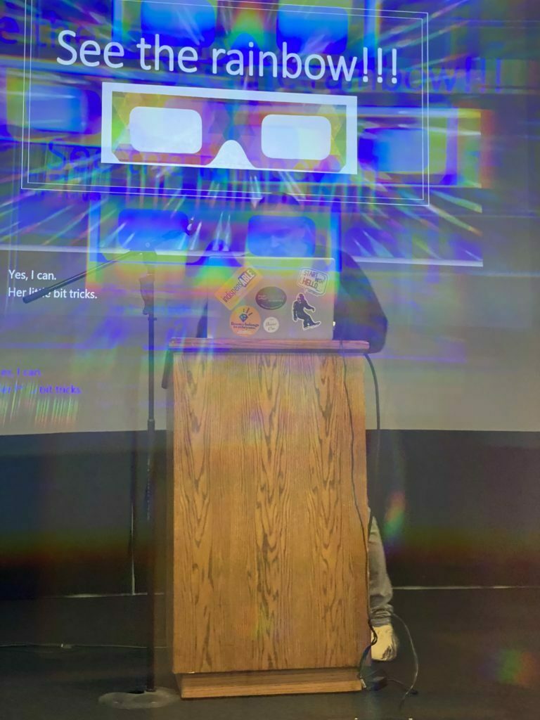 A modified image of Ryan Wolfe standing behind a podium speaking.  The image has been modified to simulate the effect of looking through 3D glasses.