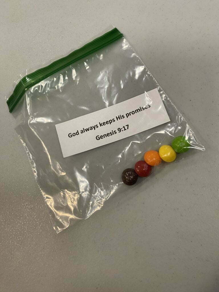 A ziploc bag containing five pieces of Skittles candy sits on a table.  Also inside of the bag is a small piece of paper that reads: "God always keeps his promises - Genesis 9:17"