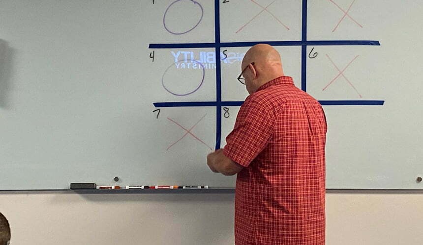 A man showcasing a Tic-Tac-Toe game on a white board as part of the curriculum.