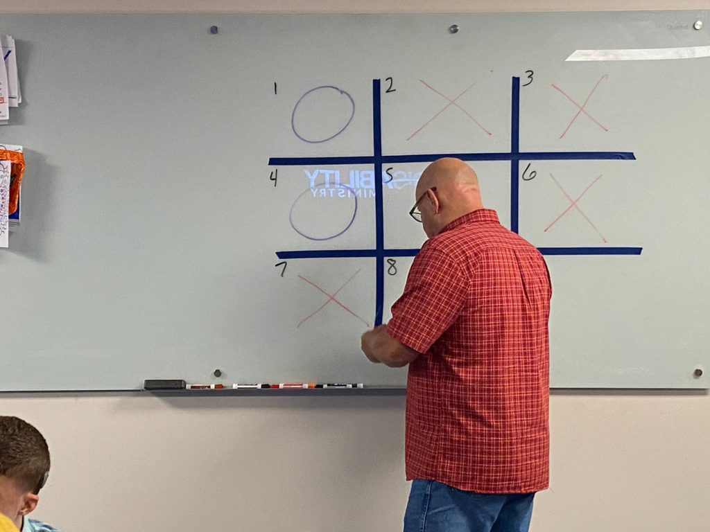 A man and a child engaging in a Tic-Tac-Toe game for educational purposes.