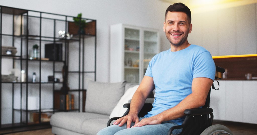 A man, seated in a wheelchair, in a living room setting.
