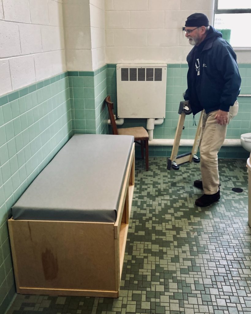 A man moving a dolly away after installing a DIY universal-sized changing table located in a restroom at a church.