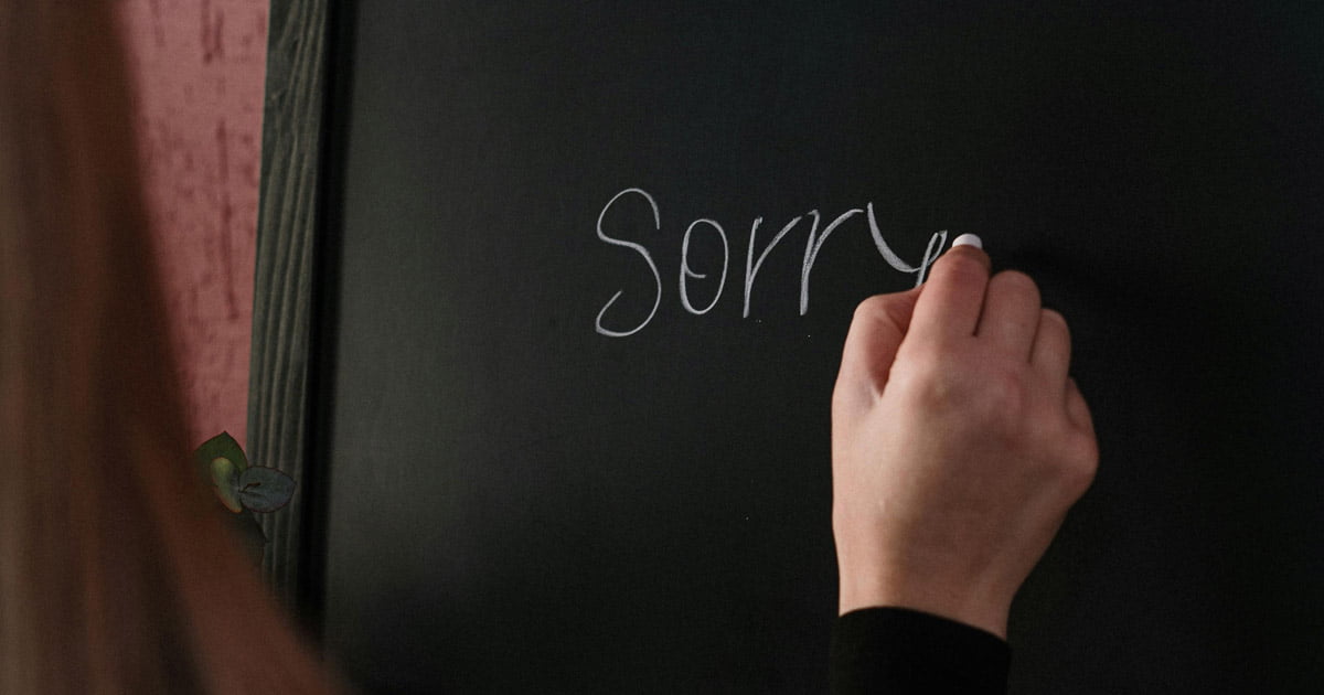 A woman writing the word sorry on a chalkboard
