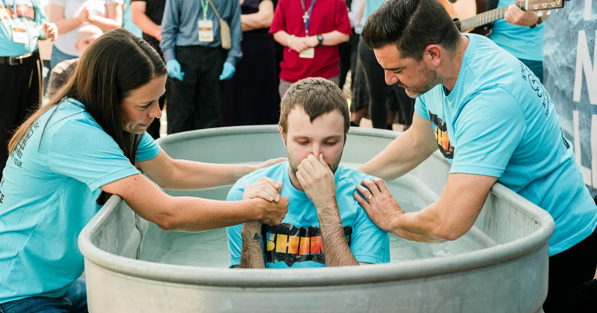 Two church volunteers assist a young man who is about to be baptized.