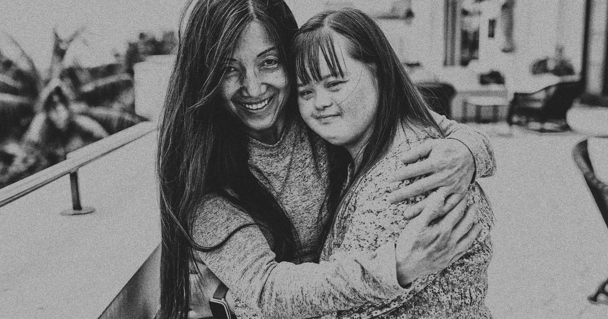 A mother hugs her daughter, who has Down syndrome, as they both smile for the camera.