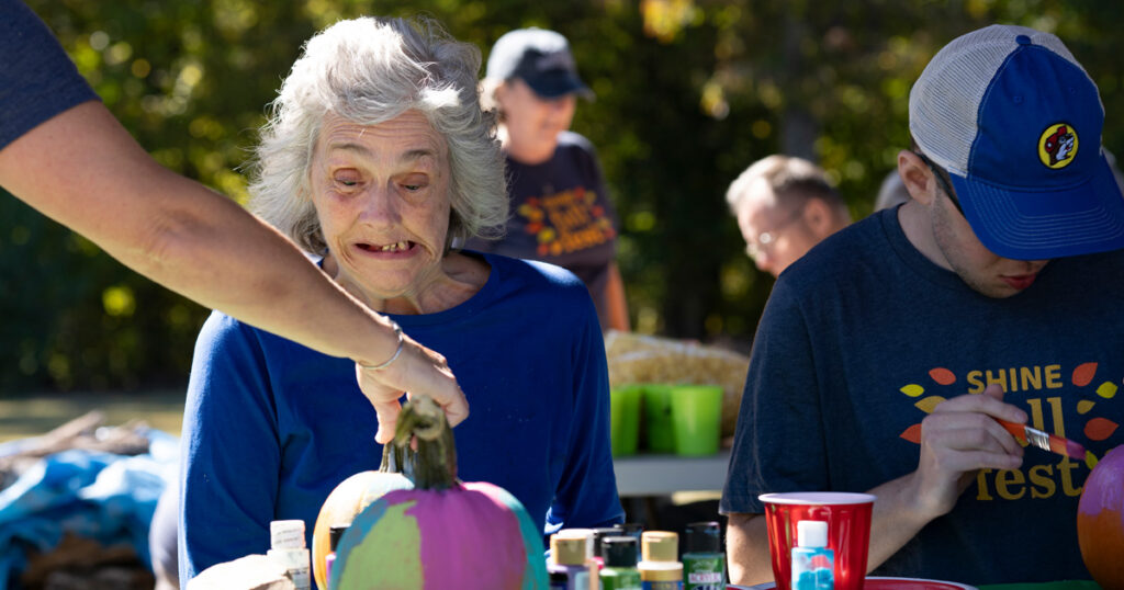 A woman is working on a painting craft at a picnic table outdoors.