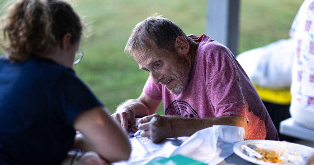 A man and young woman work on a craft activity outdoors.