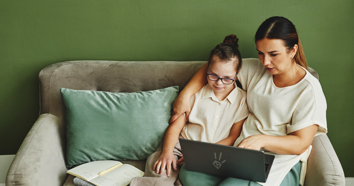 A mother and daughter sitting on the couch looking at a laptop together.