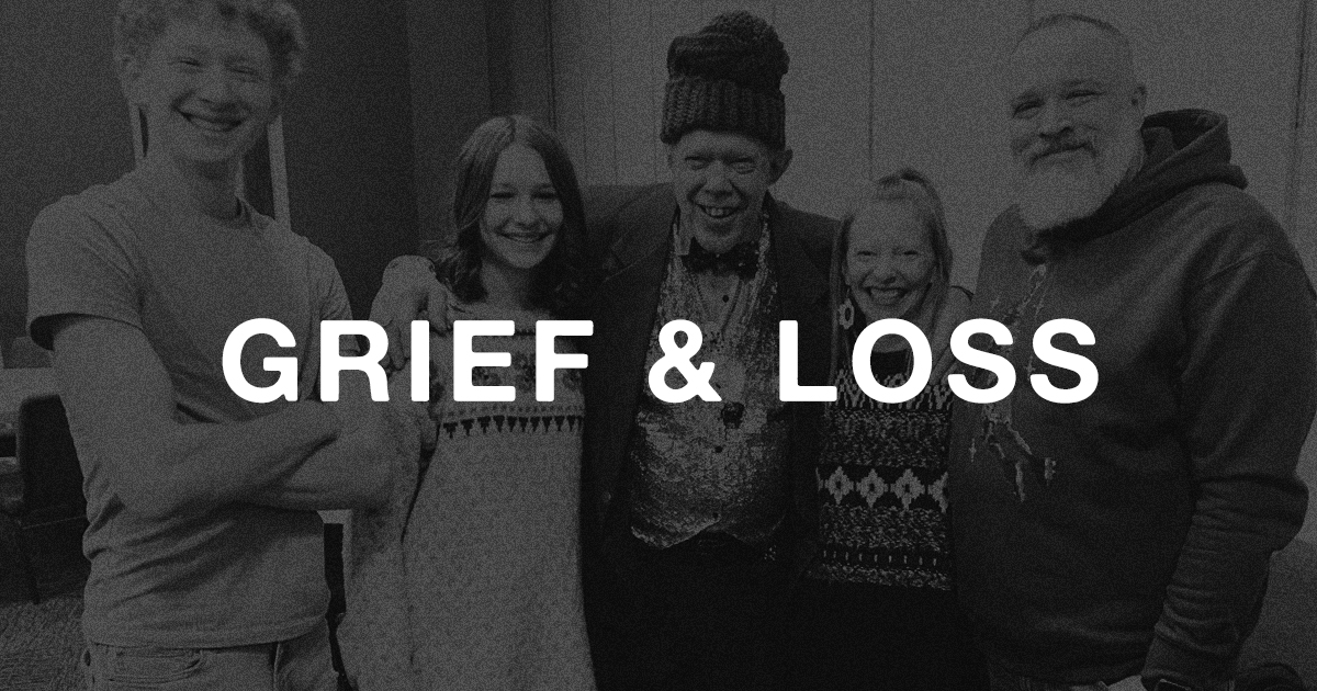 Five smiling people stand together in a black and white photo with GRIEF & LOSS boldly overlaid, reflecting unity during loss.