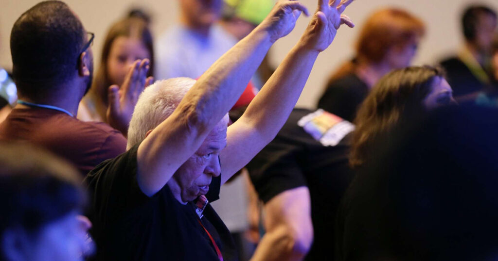 An older man worshipping at church with his hands raised.