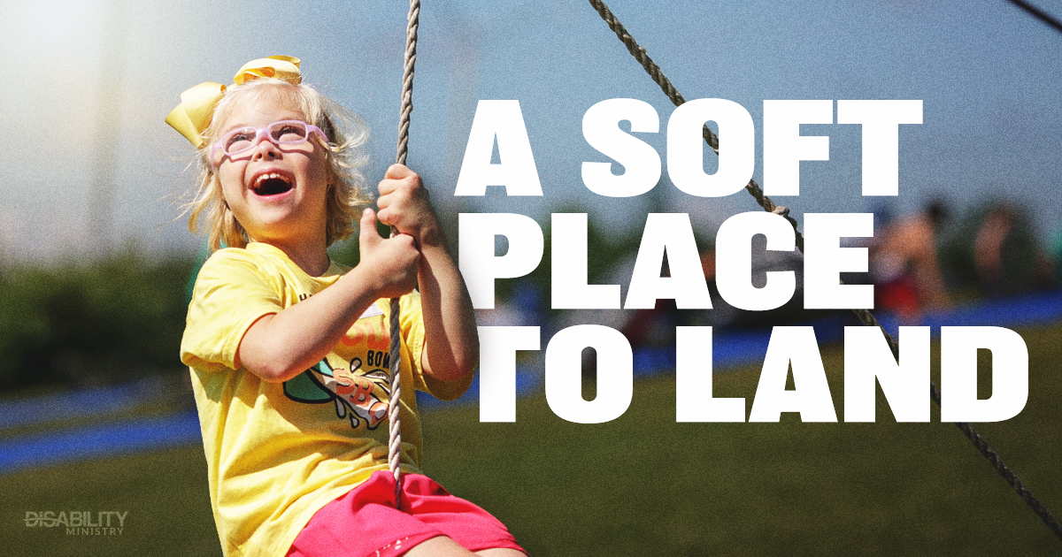 Young child wearing glasses and a yellow bow happily swings outside, surrounded by a warm, inviting atmosphere. Large text nearby says A Soft Place to Land, enhancing the sense of comfort in the scene. In the background, blurred figures and green grass suggest an active, lively outdoor setting.