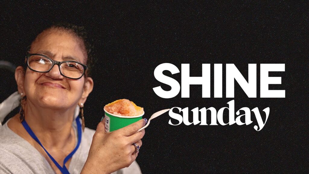 A woman wearing glasses smiles while holding a green cup of shaved ice with a wooden spoon, next to the text SHINE sunday for a disability inclusion ministry.