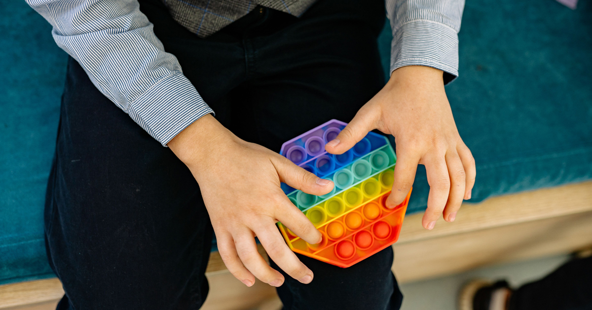 A child’s hands press the bubbles on a colorful, hexagonal silicone fidget toy, a tool often used in an inclusive church setting.